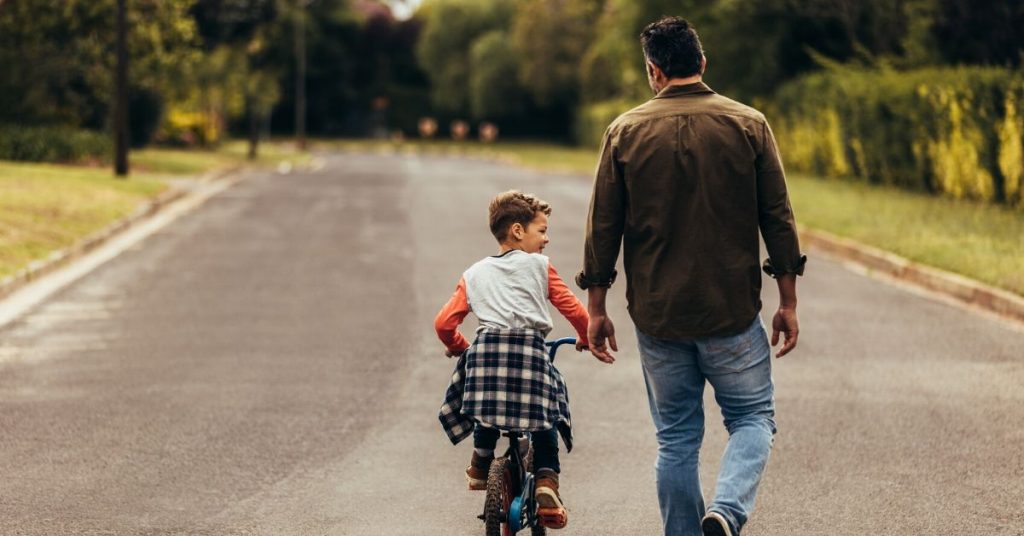 photo of a man helping his son ride a bike down the road